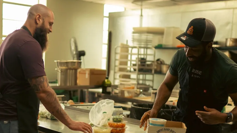 Two men in a kitchen, one holding a loaf of bread